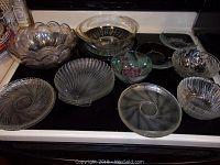 Overview of various clear glass serving bowls and dishes placed on stove top showing scalloped edges, swirl and ribbed patterns, and varied sizes.