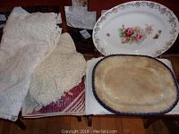 Five linens and platters arranged on chair, showing two platters and three tablecloths stacked.