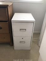 White metal file cabinet with two drawers, flush front handles, minimal wear, placed on carpet.