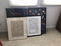 Four large framed art pieces leaning against wall including New York Times newspaper print and colorful arts festival poster