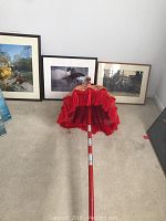 Red Bali umbrella standing upright in front of three large framed photos laid on the floor against the wall. The umbrella is open and shows red fringe.