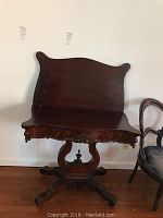 Full view of antique mahogany gaming table with curved top, pedestal base, and ornate apron.