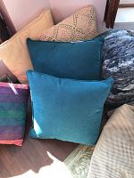 Photo of assorted needlepoint pillows with different fabrics and colors showing turquoise velvet and beige textured pillows with some shadows and sunlight
