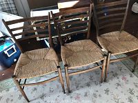 Three matching wooden dining chairs with natural rush seats and horizontal slat backs, positioned side by side on a patterned rug.