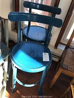 Two blue painted wooden barstools with round seats and horizontal backrests showing signs of age.