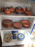 Three shelves filled with orange Bavarian lusterware including a teapot, sugar bowl, creamer, cups, saucers, and plates; blue Wedgwood octagonal luncheon plates, and additional decorative plates and a blue vase.