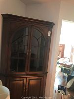 Full view of the early American style wooden corner cabinet with glass upper doors and wooden lower doors, showing overall shape and design.