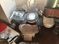 Dishware including pig-shaped platter, mugs, glass and ceramic vases, plate stand and plastic kitchen containers on a small wooden table.