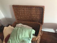Open wicker chest containing folded blankets of various colors and textures.