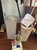 Photo showing various cleaning supplies including buckets, plant stand, broom handles and mop heads.