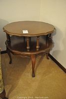 Front angle view of the round wooden side table showing two-tier shelving and carved legs