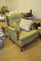 Front angled view of upholstered side chair with wood frame and damask fabric, two decorative pillows on seat.