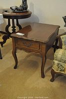 Full view of Mersman wooden side table showing drawer front, curved legs, and visible wear.