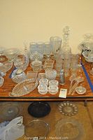 Full view of assorted clear cut glassware and serveware on a wooden table, including pitchers, drinking glasses, serving plates, and small dishes.