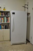 Exterior view of closed white upright freezer against wall with bookshelves