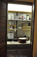 Photo showing pantry/open cabinet with Rival Crock Pot, white electric griddle, brown and white cooking pot with lid, glass containers, and more small appliances.