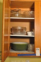 Wooden cabinet interior with glass mixing bowls, a textured glass bowl, and ceramic bowls including a green one and a small glass measuring cup.
