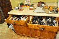 Two wooden drawers open showing kitchen cutlery and utensils inside a cabinet with a countertop above