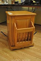 Oak cabinet showing one side with hinged magazine rack extended, detailing wood grain and spindle supports.