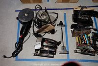 Overview of the lot showing various electric hand tools including sander, Sabre saw, grinder, and blades