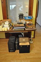 Photo showing oak case turntable, vinyl LPs, puzzles, heaters, candles, and drink set items on and under table.