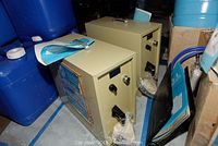 Two Aqua-Rich reverse osmosis drinking water systems placed on the floor near blue barrels, with instruction manuals on and around the units.
