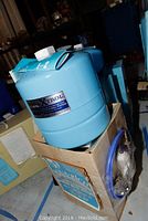 Blue Well-Xtrol branded water storage tank sitting on a cardboard box, showing the tank's label with model and brand information.