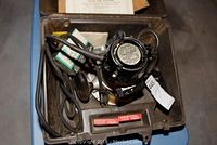 Overhead view of Craftsman wood router inside brown plastic carrying case with cables and small components.