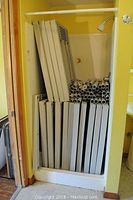 Stack of dismantled beige plastic shelving panels and hollow support tubes stored vertically in a small enclosed shower stall.