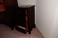 Four drawer wood nightstand with drawers partially open, dark wood finish, situated against a wall