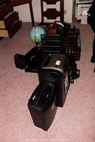 Photo showing two shredders, multiple black plastic office organizers including pen holders and paper/file holders, wooden chairs, and a globe in background.