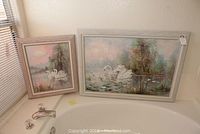 Two framed swan oil paintings placed on edge of bathtub, showing overall size and frames.