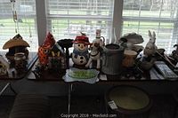 Photo of assorted garden decor items including a galvanized watering can, animal and seasonal figurines, and decorative signs on a table by the window.