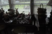 Overall view of wind chimes, garden figurines, baskets, and other decorative pieces on table by window with blinds.