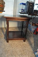 Wooden side table placed on carpet, photographed from an angle showing front and side views, details of legs and lower shelf visible.