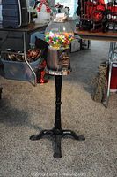 Full view of the carousel gumball machine with metal stand and glass globe containing colorful gumballs on carpeted floor surrounded by other household items.