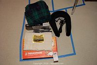 All items included in lot arranged on floor: foot massager box and plaid cover, neck massager, Thermophore heat pack with cloth cover.