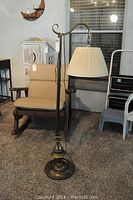 Full view of the brass finish floor lamp standing next to a beige rocking chair and other furniture.