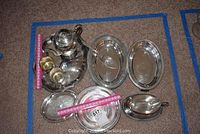 Overview of 10 silver plated serving pieces including teapot, cups, trays, and bowls displayed on carpet with measuring rulers for scale.