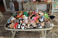 Wide view of table with numerous Ty Beanie Babies and other stuffed animals arranged closely, showing variety of colors and species.