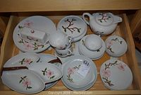 Top-down view of set showing dinner plates, butter dish, cups, saucers, dessert bowls, dessert plates, and teapot with floral design arranged in drawer.