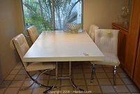Full view of the white rectangular table with four white leather chairs around it, showing the leaf extension in the center of the table.