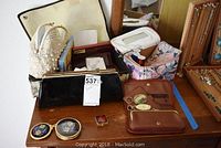 Wide shot of all vintage women's accessories arranged on wooden surface including purses, wallets, pocket mirrors, makeup bag, reading glasses