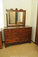 Front view of wooden dresser with mirror attached showing nine drawers and decorative top of mirror.