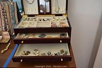 Opened wooden jewelry box showing top compartment with divided slots, ring rolls and parts of two drawers.