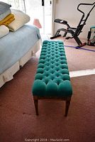 Full length top view of the green tufted velvet bench next to a bed and exercise equipment