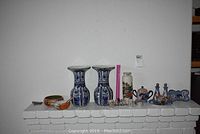 Wide shot of Asian inspired porcelain and ceramic decorative items on a white brick mantelpiece, showing vases, spoon rests, salt and pepper shakers, oil and vinegar set and other items