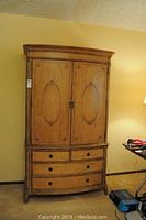 Front view of closed wooden armoire with decorative oval panels on doors and four drawers below