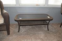 Outdoor coffee table with dark brown wicker-look frame and clear glass top, rectangular with rounded corners, shown from front.
