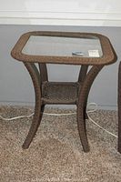 Front view of the glass topped outdoor side table with wicker-look frame showing curved legs and lower shelf.